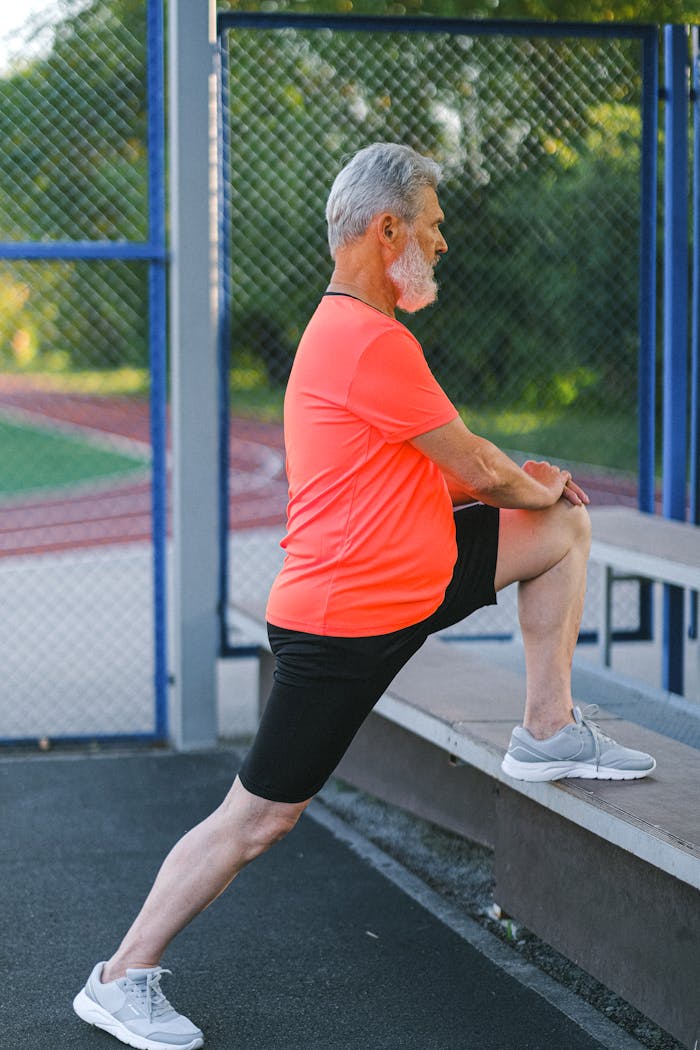 Elderly man in activewear stretches at an outdoor stadium, focusing on fitness.