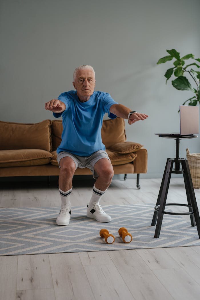 about-02 A senior man performing squats with dumbbells on a mat indoors for a healthy lifestyle.